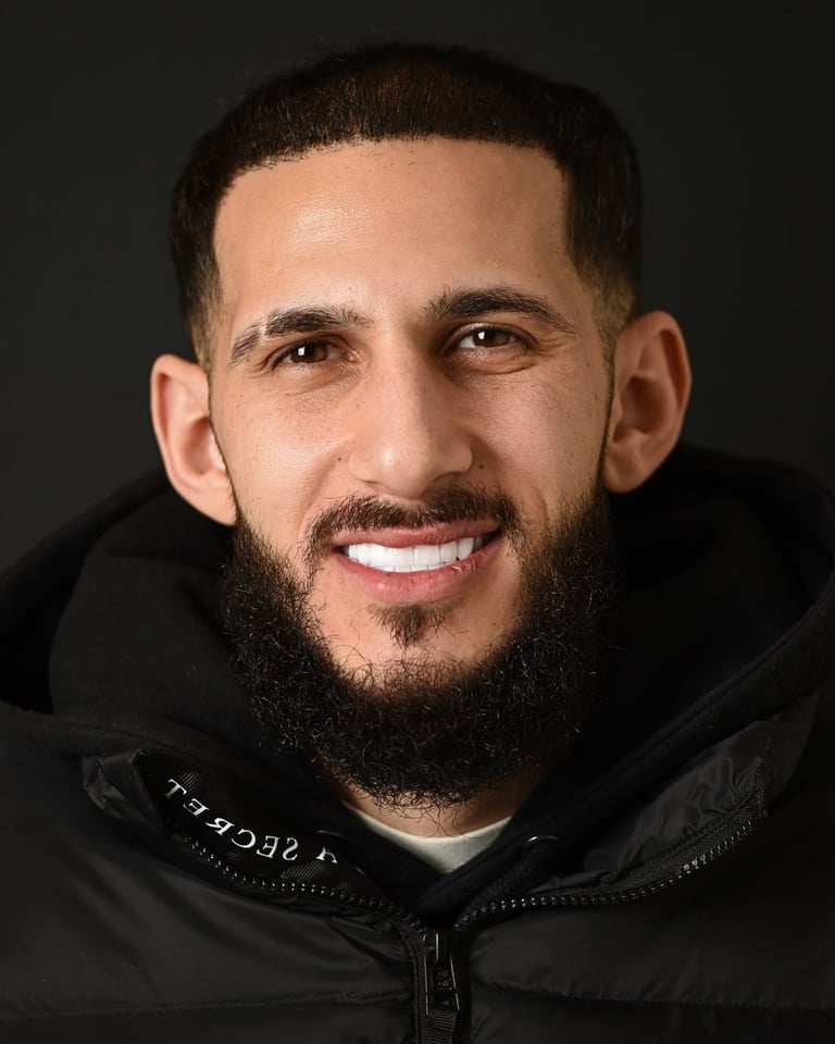 Portrait of a man with dark hair and a thick black beard wearing a black jacket, smiling warmly and showing bright white teeth after dental restoration at Smile Center Turkey.