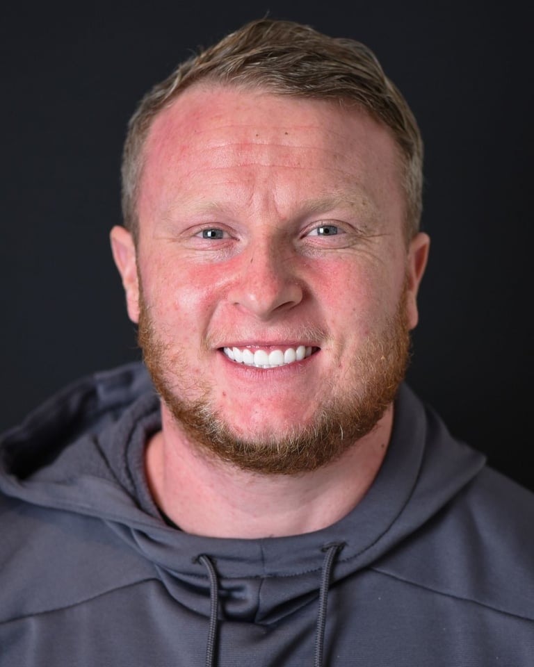 Portrait of a man with short light brown hair and a trimmed beard, wearing a grey hoodie, smiling widely and showing bright white teeth after dental restoration at Smile Center Turkey.