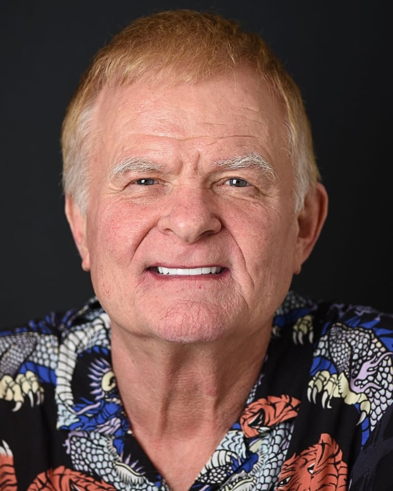 Portrait of an older man with strawberry blond hair wearing a brightly patterned floral shirt, smiling gently and showing straight white teeth after dental restoration at Smile Center Turkey.