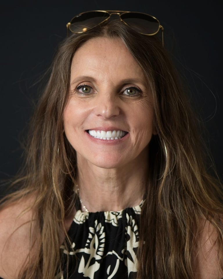 Portrait of a woman with long brown hair wearing glasses on her head and a black-and-white patterned halter top, smiling widely and showing bright white teeth after dental restoration at Smile Center Turkey.
