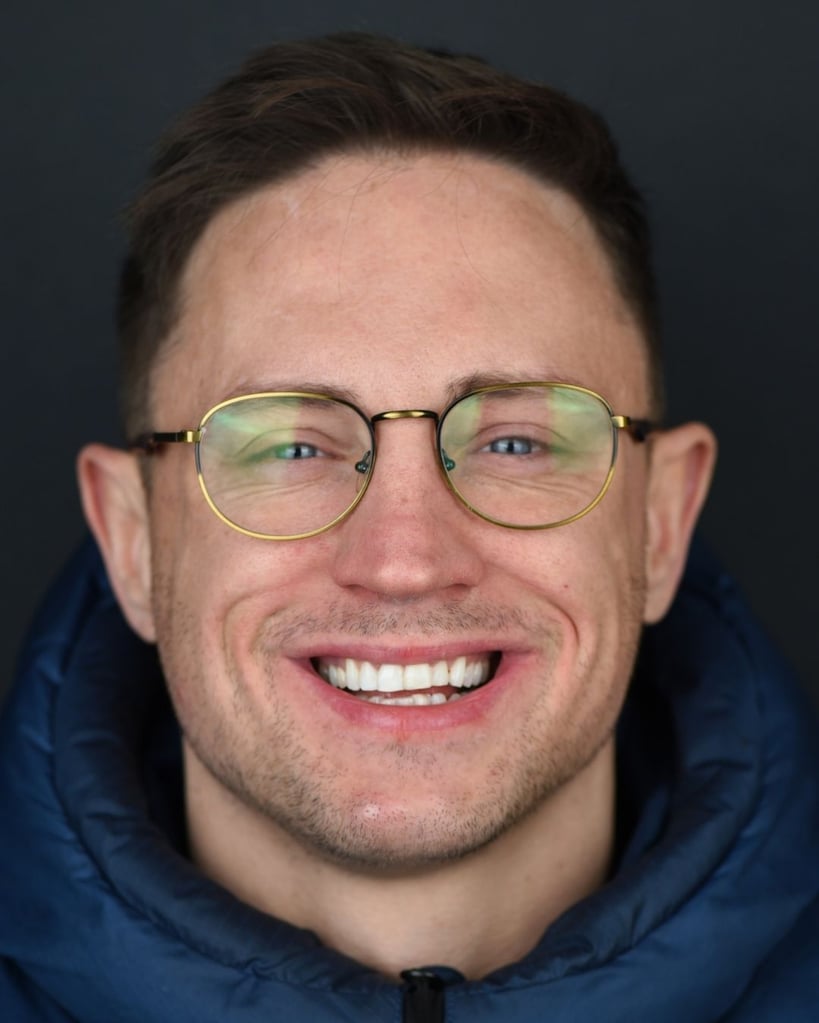 Portrait of a man with short dark brown hair wearing glasses and a dark blue jacket, smiling widely showing a gap between his front teeth before dental restoration at Smile Center Turkey.