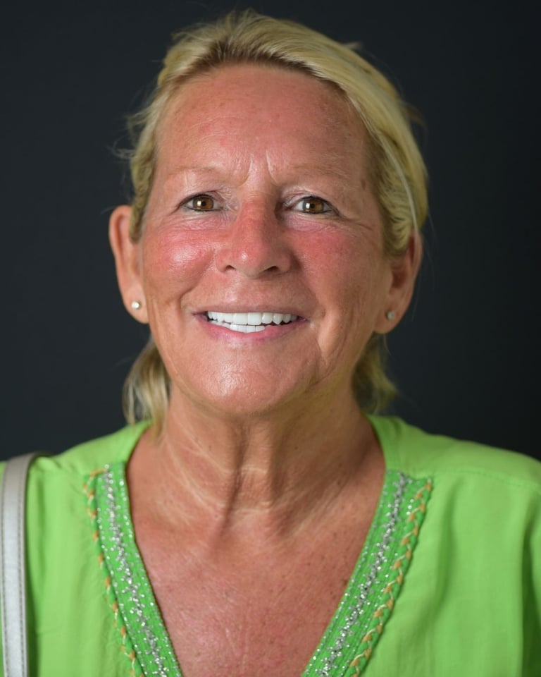 Portrait of an older woman with blonde hair tied back, wearing a green top with beaded details, smiling warmly and showing bright white teeth after dental restoration at Smile Center Turkey.
