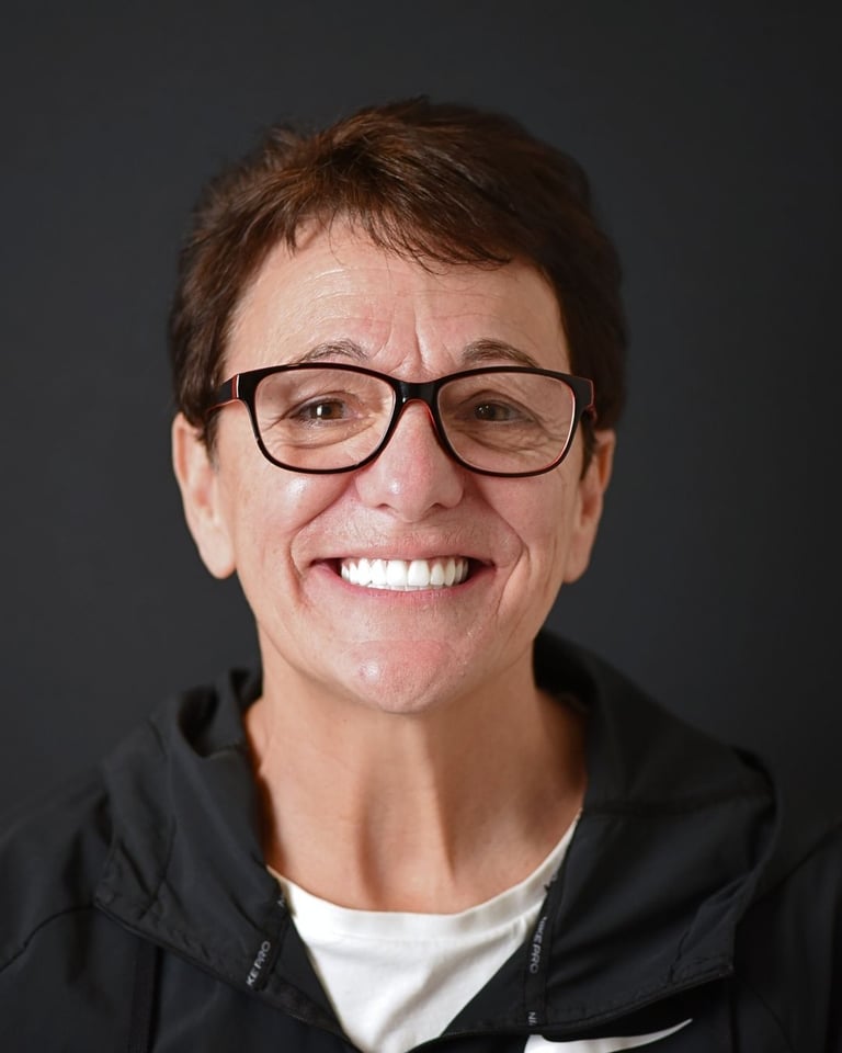 Portrait of a woman with short dark hair wearing glasses and a black jacket, smiling widely and showing bright white teeth after dental restoration at Smile Center Turkey.