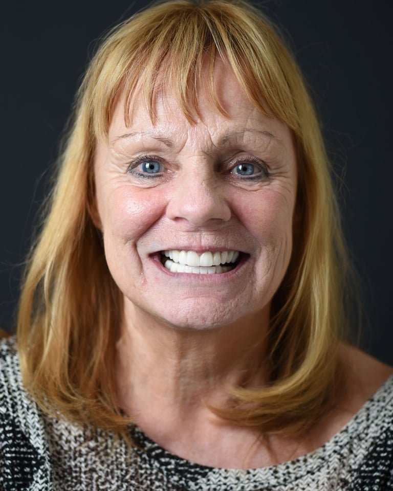 Portrait of a middle-aged woman with strawberry blonde hair and bangs, wearing a patterned blouse, smiling widely and showing bright white teeth after dental restoration at Smile Center Turkey.