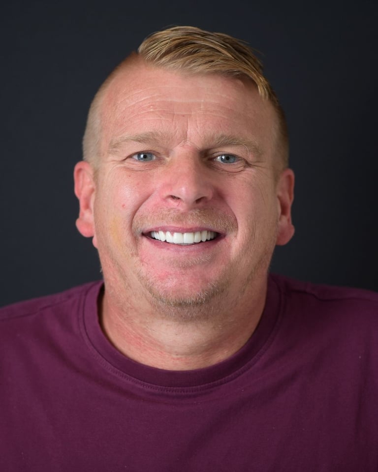 Portrait of a man with short blond hair swept to the side, wearing a maroon shirt, smiling broadly and showing straight white teeth after dental restoration at Smile Center Turkey.