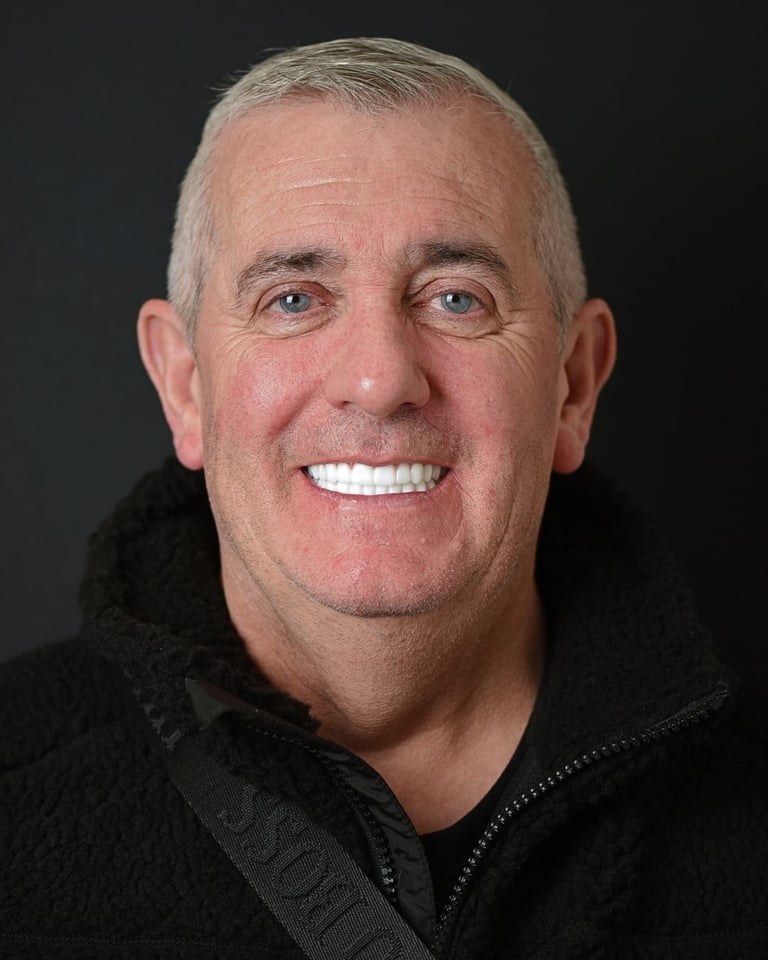 Portrait of an older man with short grey hair wearing a black fleece jacket and a black strap across his chest, smiling broadly and showing bright white teeth after dental restoration at Smile Center Turkey.