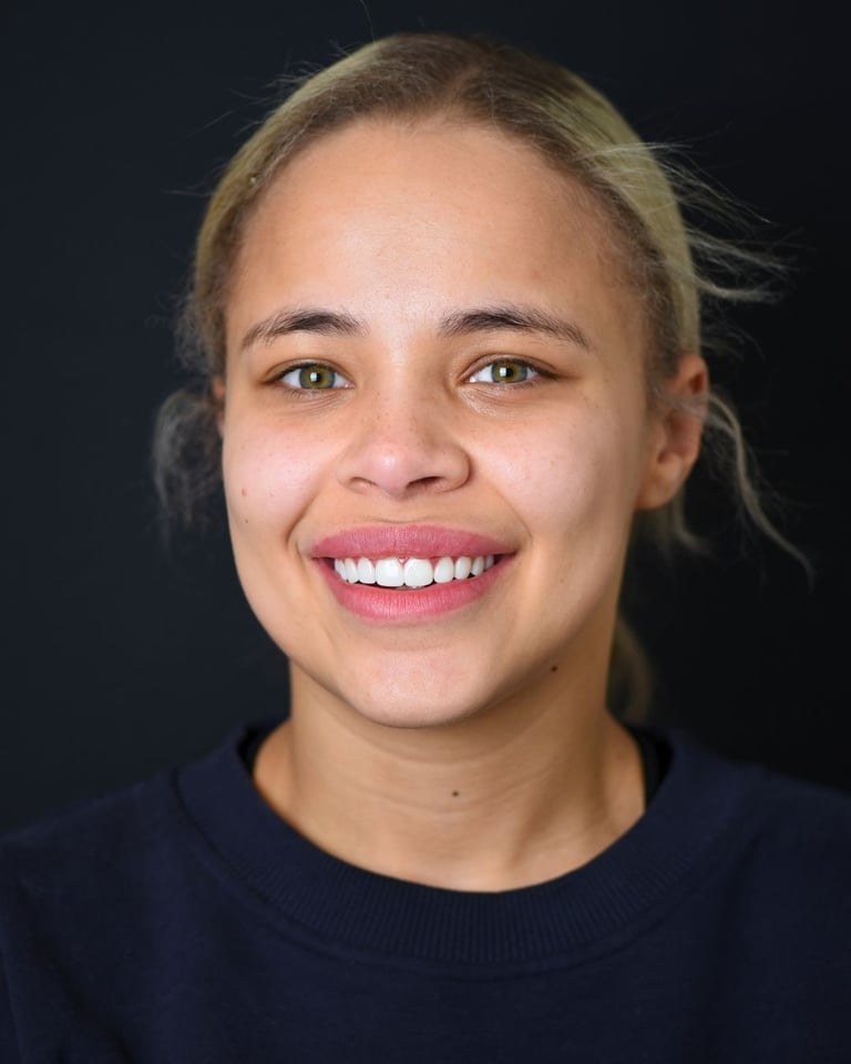 Portrait of a young woman with dark hair tied back, wearing a dark blue sweater and a small dark birthmark near her left eye, smiling gently and showing straight white teeth after dental restoration at Smile Center Turkey.